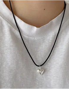 Nahaufnahme eines silbernen Herzanhängers mit schwarzer Kordelkette auf einem weißen T-Shirt
