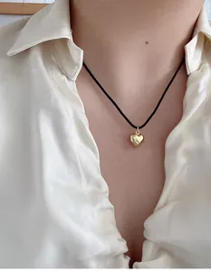 Detailaufnahme der herzförmigen Goldkette mit minimalistischer schwarzer Kordel