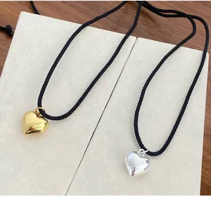 Nahaufnahme von gold- und silberfarbenen Herzanhängern mit minimalistischen schwarzen Kordeln