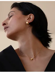 Dettaglio di orecchini a cerchio dorati opachi e collana indossati da una modella
