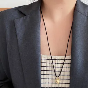 Minimalistische goldene Herz-Halskette mit schwarzer Kordel auf eleganter Kleidung