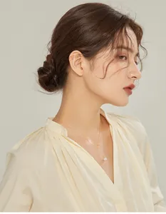 Detail of a gold Y-shaped necklace with a single pearl pendant worn on a pleated V-neck