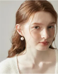 Dettaglio di orecchini di perle bianche rotonde con ganci dorati su una modella
