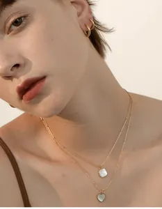 Detalle de collares dorados en capas con colgantes de nácar blanco cuadrados y de corazón