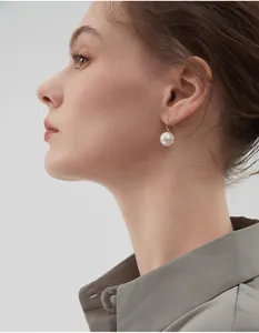 Close-up of a large round grey pearl drop earring on a model with golden ear hooks