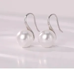 Macro detail of round white pearl earrings with minimalist silver-tone hooks