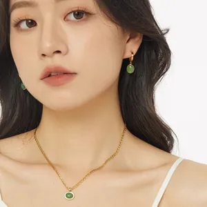 Golden necklace and earrings set with oval green aventurine stones on a model
