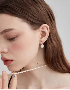 Close-up of French vintage C-shape pearl earrings and heart pendant necklace on a model