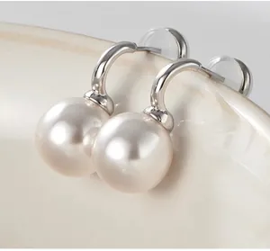 Close-up of elegant C-shaped silver earrings with large white round pearls on a ceramic bowl