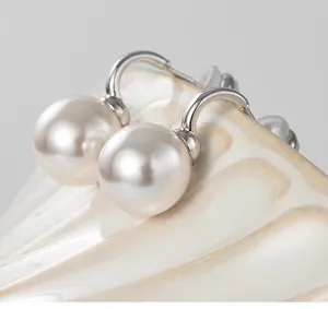 Detailed close-up of cream round pearls set in U-shaped silver metal earrings