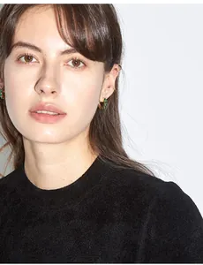 Close-up of luxury gold hoop earrings with emerald green zircons on female model ear