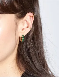 Macro shot of emerald green gemstone earrings and textured gold ear cuffs on model