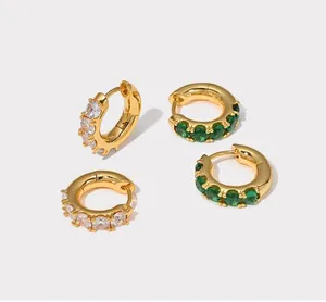 Close-up of small gold huggie hoop earrings with emerald green and white zircon stones
