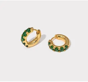 Close-up of golden hoop earrings featuring micro-paved emerald green oval crystals
