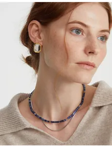 Dettaglio di orecchini dorati con cristallo e collana di perline blu indossati sul modello