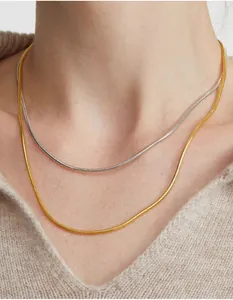 Dettaglio di catene a serpente oro e argento sovrapposte su un maglione beige