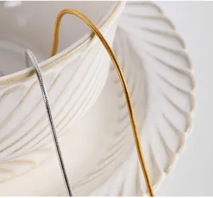 Dettaglio di catene a serpente da 1mm oro e argento su una tazza di ceramica bianca