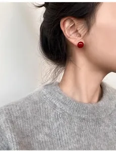 Gros plan d'une boucle d'oreille rouge brillante portée sur l'oreille avec un pull gris