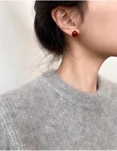 Gros plan d'une boucle d'oreille sphérique rouge brillant portée sur l'oreille d'un modèle