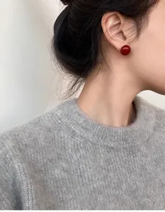 Détail de boucles d'oreilles perles rouges minimalistes portées par un mannequin en hiver
