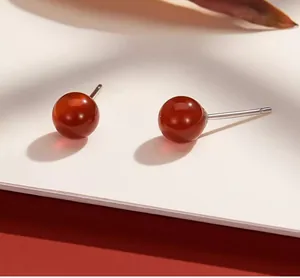 Dettaglio di orecchini a lobo in agata rossa con perni in argento su scheda minimalista