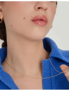 Close-up of 18K gold plated satellite chain necklace worn by a model with blue collar
