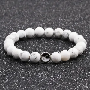 Nahaufnahme von weißen Türkisperlen mit Marmortexur und Yin-Yang-Symbol-Perle am Armband
