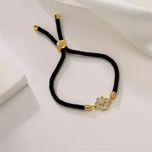 Detail of adjustable black woven rope bracelet with gold clover charm and zircon stones