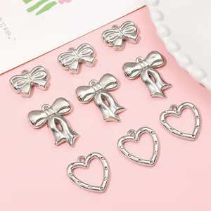 Silver bow and heart-shaped DIY pendants for necklaces on a soft pink background