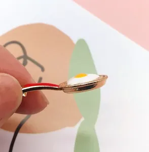 Cute golden frying pan enamel pin with sunny-side-up egg and bright red handle