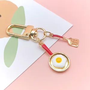 Macro detail of golden keychain with miniature frying pan, fried egg and spatula charms