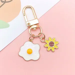 Close-up of golden keychain featuring enamel fried egg and sunflower charms on pink background