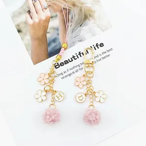 Pink floral keychain with plush pompom and gold enamel letters on a minimalist background
