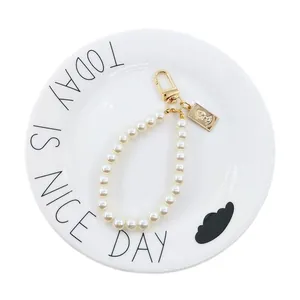 Vintage pearl keychain featuring gold portrait relief pendant and metal clasp on white dish
