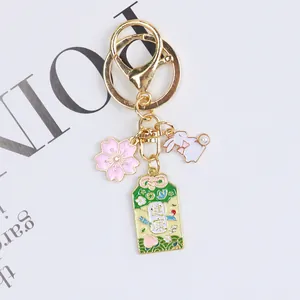 Detail of a gold keychain featuring a pink enamel cherry blossom and pearl rabbit charm