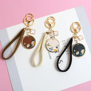Detailed embroidery of daisy floral keychains in brown, beige, and black leather finish