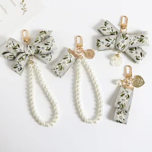 Detail of floral ribbon keychains with pearls and shell charms on a white surface