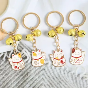 Détail de quatre porte-clés chat Maneki Neko avec clochettes dorées sur fond texturé