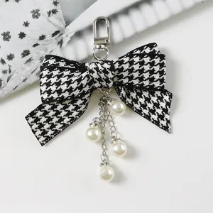 Detail of checkered ribbon bow keychain with elegant hanging white pearls on white background