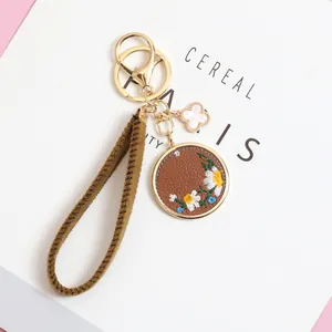 Detailed close-up of embroidered daisy PU leather keychain with gold lobster clasp and strap