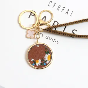 Detailed shot of embroidered daisy on leather keychain with gold lobster clasp