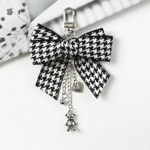 Detail of houndstooth bow keychain with silver bear and heart charms on a white desk