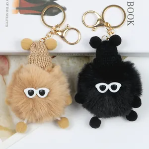 Dettaglio di portachiavi a pompon in peluche kaki e nero con occhiali e cappelli