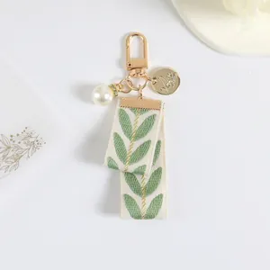 Detailed view of cream ribbon keychain with green leaf embroidery and pearl charm