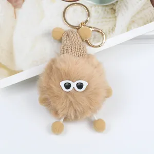 Dettaglio portachiavi a pompon con cappellino e occhiali da sole su sfondo morbido