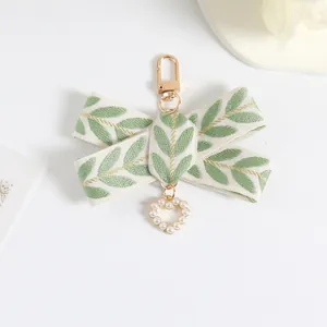 Detail of ribbon bow charm with green leaf embroidery and heart-shaped pearl pendant