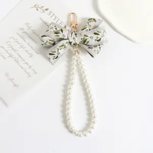 Detailed view of beige floral embroidery bow keychain with white pearls and gold clasp