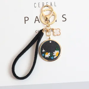 Detail of embroidered daisy keychain with gold lobster clasp and black leather pendant