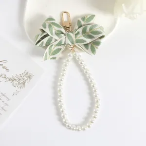 Detail of floral beige bow keychain with gold hook and round white pearl loop strap