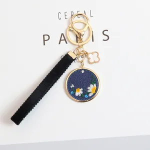 Detailed macro view of navy blue PU leather keychain with embroidered daisy and gold hardware